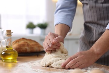 Fototapeta premium Making bread. Man kneading dough at wooden table in kitchen, closeup