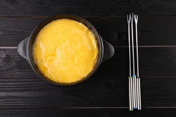 Fondue pot with melted cheese and forks on black wooden table, top view