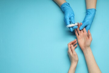 Diabetes. glucose testing. Doctor using lancet pen on light blue background, top view. Space for...