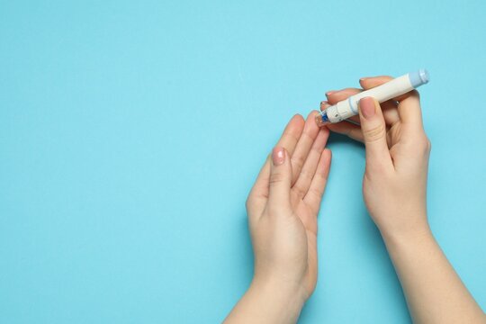 Diabetes. glucose testing. Woman using lancet pen on blue background, top view. Space for text