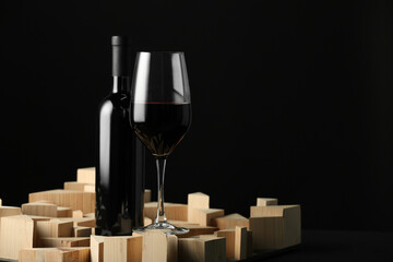 Stylish presentation of red wine in bottle and wineglass on black background, space for text