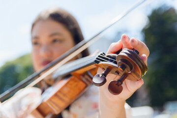 closeup of blurred unrecognizable woman tuning violin, focus on hand on pegs