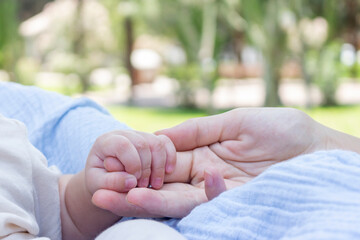 Detalle de unas manos de una madre agarrando la mano de su bebé en un parque en un día soleado