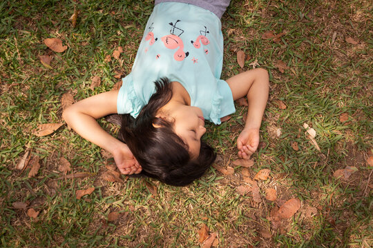 Ni&ntilde;a sonriendo de siete a&ntilde;os echada sobre el pasto en el parque en un d&iacute;a soleado rodeada de naturaleza y hojas de los &aacute;rboles