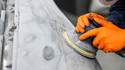 A mechanic sands the putty on a car body with a machine. Repair after an accident. 