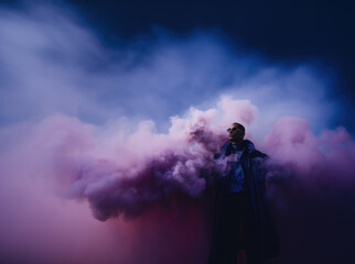 Cinematic appearance of a man among colored clouds. Mysterious person among smoke bombs