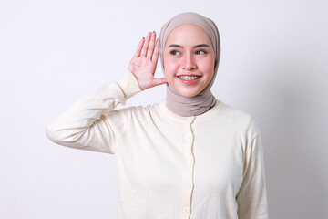 Beautiful muslim woman with dental braces puts hand near ear to listening something over white...