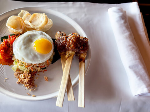 Indonesian Fried Rice Nasi Goreng served with soya sauce, chilli paste sambal, sunny side up, satay, sate, chicken skewer and kerupuk crackers