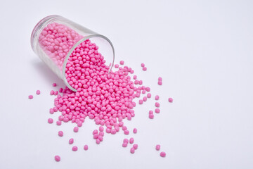 pink masterbatch granules spilled from a shot glass, isolated on a white background. polymer...