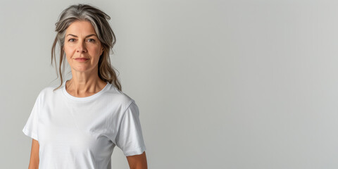 Grey haired woman in white tshirt in front of white wall with room for artwork