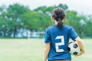 運動場でサッカーボールを持つサッカーファン・サポーターの日本人女性の後ろ姿

