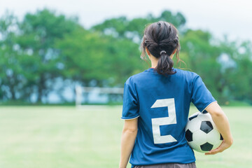 運動場でサッカーボールを持つサッカーファン・サポーターの日本人女性の後ろ姿  © buritora