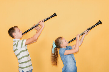 Boy and girl musicians playing the clarinet, on a yellow background.