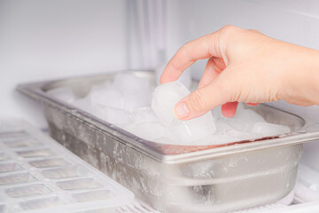The girl collects frozen ice cubes from the freezer to prepare soft drinks.