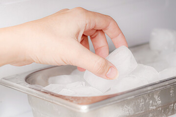 The girl takes frozen ice cubes from the freezer with her hand to prepare soft drinks.