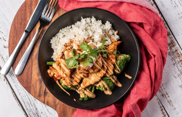 A top-down view of a bowl of Peri Peri Chicken in a round bowl with broccoli, with rice and spicy sauce