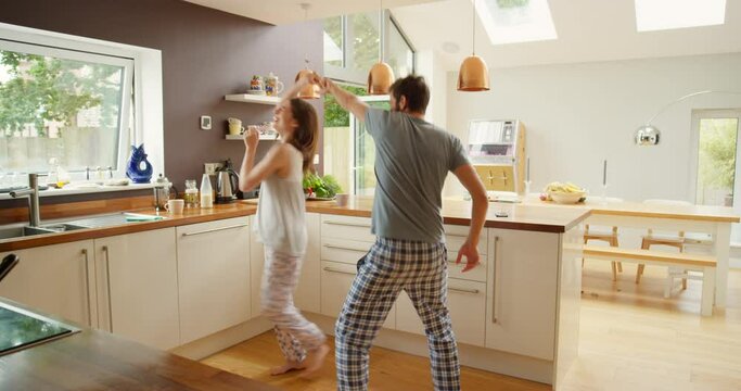 Dance, love and morning with couple in kitchen for celebration, happiness and bonding together. Wake up, energy and romance with crazy man and woman in pyjamas at home for music, support and date