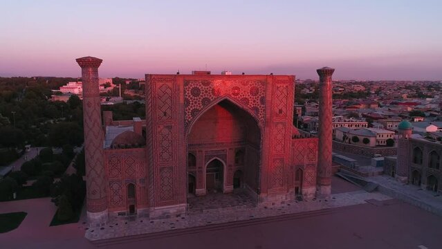 A drone flies near a complex Bibi-Khanym Mosque in Samarkand, Uzbekistan. The building is illuminated by the pink dawn light. Cloudless morning.