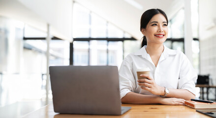 Image of young beautiful joyful woman smiling and relaxing while working with laptop in office