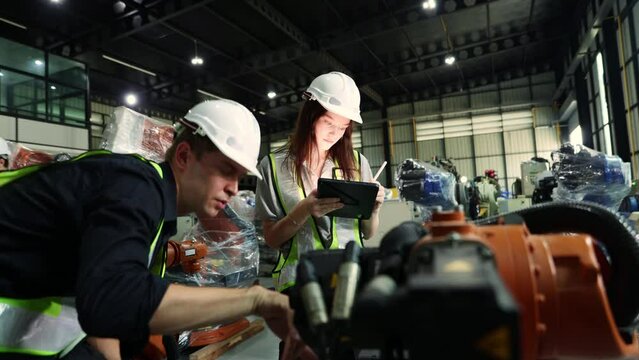 Male and female electrician robot engineer inspecting new welding robot testing electrical installation process with laptop electronic automation system setup in warehouse modern business industry 4.0