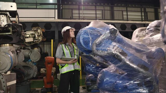 Female engineer walking around carefully inspecting the new robot zone in the warehouse robot is covered clear dustproof plastic sealed and the robot inspection service is waiting electrical testing.