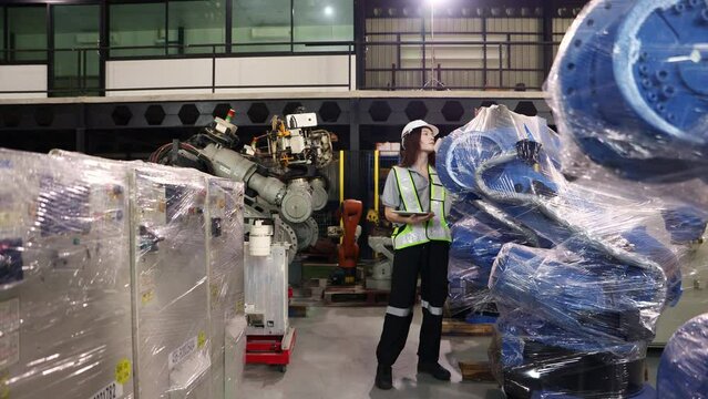 Female engineer walking around carefully inspecting the new robot zone in the warehouse robot is covered clear dustproof plastic sealed and the robot inspection service is waiting electrical testing.