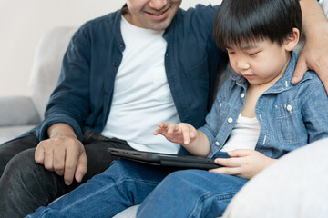 Happy single father playing teach using tablet with the little boy. family is happy and excited in the house. Father and son having spending time together, Good daddy , addiction fix, handle, control - Powered by Adobe