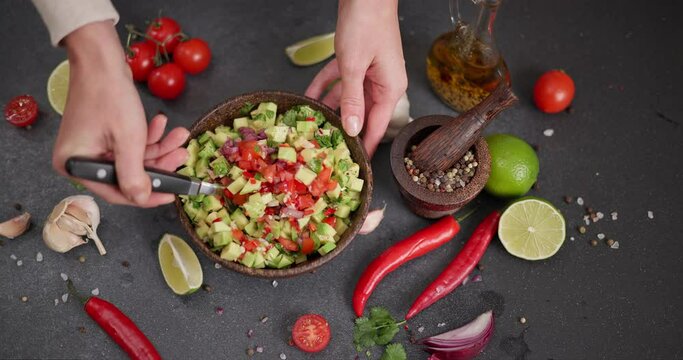 Salsa recipe - Woman mixing Chopped ingredients in wooden bowl - avocado, onion, cilantro and pepper