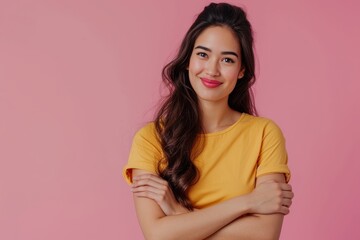 Obraz premium Beautiful Latin woman in her 20s with a joyful smile wearing a yellow shirt poses with folded hands on a pastel pink background