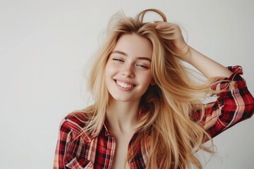 Fototapeta premium Blond girl gently touches her hair with a happy expression dressed casually in front of a white background