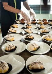 hotel employees are preparing snack cakes on plates before the meeting. Many rows of plates with buffet snacks.