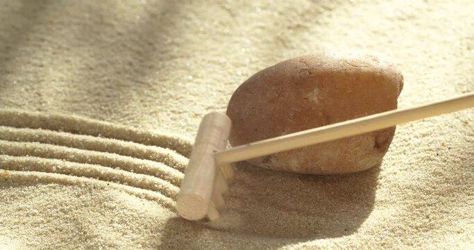 Close-up making zen garden with sand and stone using mini bamboo wooden rake