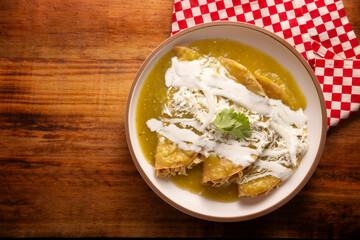 Green enchiladas. Typical Mexican dish made with a folded or rolled corn tortilla filled with shredded chicken and covered with spicy green sauce, cream, grated cheese and onion.