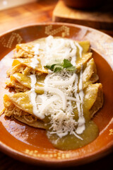 Green enchiladas. Typical Mexican dish made with a folded or rolled corn tortilla filled with shredded chicken and covered with spicy green sauce, cream, grated cheese and onion.