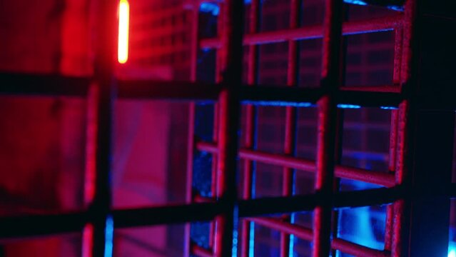 Thriller jail lit with ambient red and blue neon light. Cinematic metal bars in scary dungeon cell for torture. Abandoned prison. Creepy cage underground. Ancient underground chamber. Old prison grate
