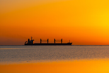 Silhouette of a container ship sailing on the waves of the Red Sea during sunrise. 