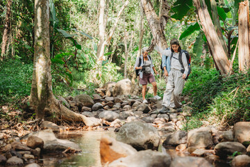 Young female backpacker group traveling in wild forest, Attractive girl traveler look around and explore while walk in nature wood with happiness and fun during holiday vacation trip.