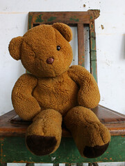 Teddy bear sitting on the wooden chair. 