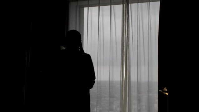 Silhouetted agitated troubled man on phone call pacing in moody dimly lit room