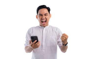 Happy Asian Muslim man holding mobile phone, gesturing yes with clenched fist, getting good news isolated on white background. Ramadan and Eid Fitr celebration concept