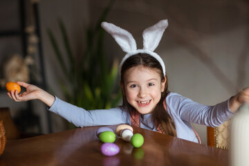 happy child girl playing with Easter eggs at table at home