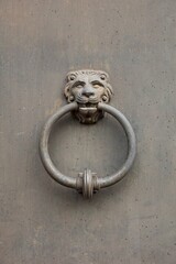 Closeup of rustic lion-head door knocker on a metal door.
