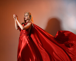Close up portrait of beautiful blonde model wearing flowing red silk toga gown and crown, dressed...
