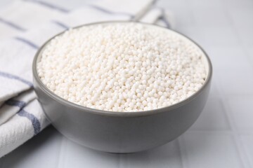 Tapioca pearls in bowl and towel on white tiled table, closeup