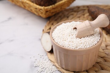 Tapioca pearls in bowl and cassava roots on white table, closeup. Space for text