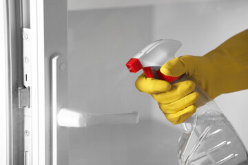 Woman with spray bottle and microfiber cloth cleaning window, closeup