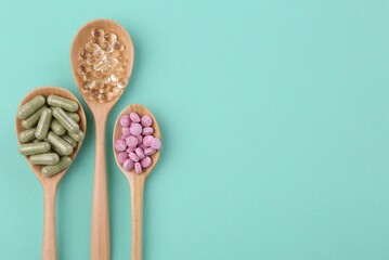 Different vitamin pills in wooden spoons on turquoise background, flat lay. Space for text