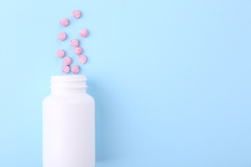 Jar with vitamin pills on light blue background, top view. Space for text