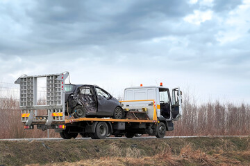 A side-impact collision leaves a car in need of a tow truck.  The car is severely damaged and may be beyond repair. A modern black Japanese hatchback is being hauled away by a tow truck on the highway