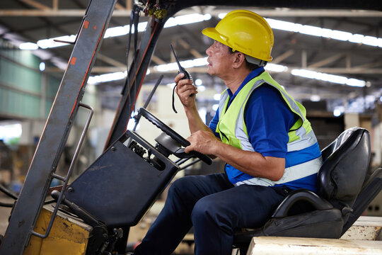 senior worker using walkie talkie and driving forklift truck in the factory